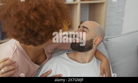 Interrassisches Paar teilt sich eine liebevolle Umarmung auf einer Couch in einem städtischen Wohnraum. Stockfoto