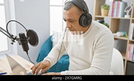 Reifer hispanischer Mann mit Kopfhörern, der Laptop im Innenraum des Radiostudios benutzt. Stockfoto