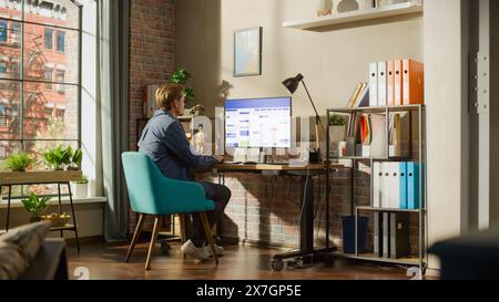 Konzept für Remote-Arbeit: Mann, der einen Desktop-Computer mit Office-Software verwendet, um den Zeitplan im Kalender zu überprüfen. Junge Männer planen Geschäftstreffen in stilvollem Loft-Apartment mit großem Fenster. Stockfoto