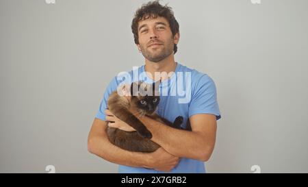 Ein zufriedener junger Mann umarmt eine siamesische Katze, beide isoliert auf einem sauberen weißen Hintergrund. Stockfoto