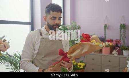 Ein junger hispanischer Mann auf einer Schürze arrangiert Blumen in einem Geschäft und zeigt seine Floristik-Fähigkeiten. Stockfoto