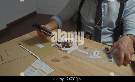 Ein junger hispanischer Mann untersucht Beweise in einem Detektivbüro mit Fotos, Dokumenten und Gegenständen, die auf einem Schreibtisch verteilt sind. Stockfoto