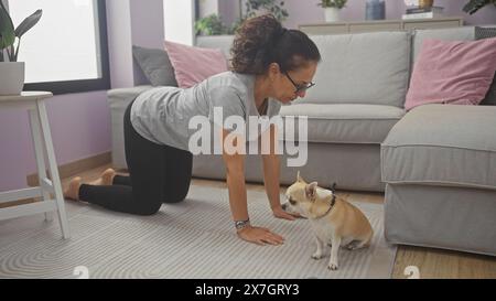 Eine Frau mittleren Alters in einer Plankenposition interagiert mit einem chihuahua in einem gemütlichen Wohnzimmer. Stockfoto