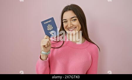 Lächelnde junge Frau, die einen US-Pass vor einem rosa isolierten Hintergrund hält. Stockfoto