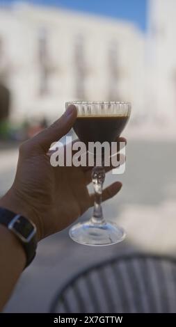 Eine Outdoor-Szene mit einem Mann, der in apulien ein Glas schwarzen Kaffee hält und das elegante Getränk vor einer verschwommenen Kulisse präsentiert. Stockfoto