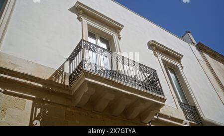 Detaillierte Ansicht der traditionellen italienischen Architektur in lecce, apulien, mit einer weißen Gebäudefassade mit kunstvollen Eisenbalkonen unter klarem blauem Himmel. Stockfoto