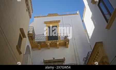 Ein bezaubernder Blick auf die Straße in gallipoli, apulien, italien, zeigt alte Gebäude mit Balkonen und einem klaren blauen Himmel. Stockfoto