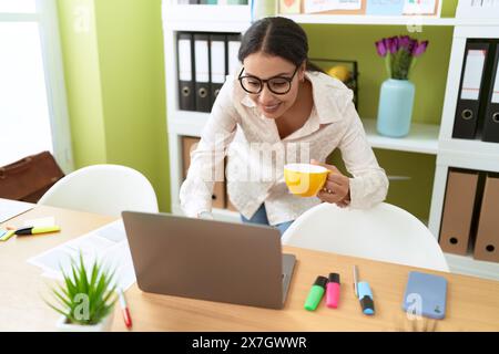 Junge arabische Geschäftsfrau, die ihren Laptop benutzt, um Kaffee im Büro zu trinken Stockfoto