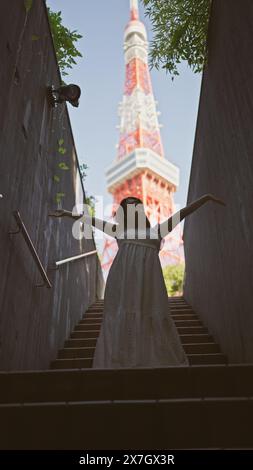 Ein faszinierendes Bild der wunderschönen hispanischen Frau in Brille, die auf einer Treppe am tokioter Turm steht. Das berühmte Wahrzeichen von tokio lädt zum Blick auf die Stadt ein Stockfoto