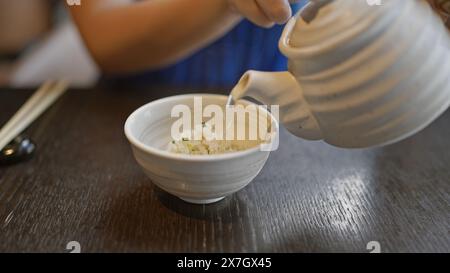 Eine junge Frau, die kochendes Wasser im Restaurant in eine Reisschale gibt Stockfoto