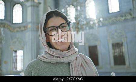 Die lächelnde Frau trägt Hijab im kunstvollen Inneren der istanbuler Moschee und verkörpert kulturelle Vielfalt. Stockfoto