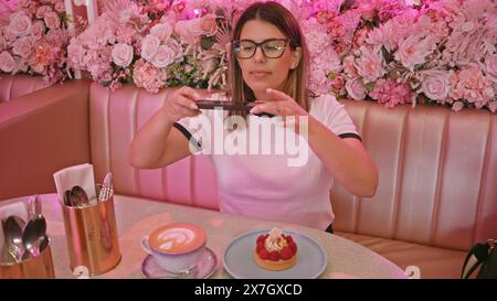 Erwachsene Frau fotografiert Desserts in einem pinkfarbenen Café Stockfoto