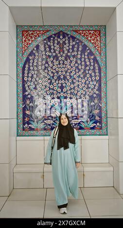 Eine junge Frau im traditionellen Hijab posiert vor kunstvollen islamischen Mosaikfliesen in einer Moschee in abu dhabi, die die Konvergenz der Kultur, Reli, darstellt Stockfoto