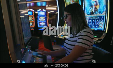 Junge Erwachsene hispanische Frau, die einen Spielautomaten in einem Casino spielt, konzentriert und begierig darauf ist zu gewinnen. Stockfoto