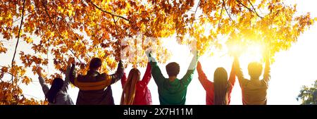 Gruppe glücklicher Freunde, die bei Sonnenuntergang mit erhobenen Händen stehen Stockfoto