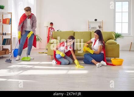 Eltern und Kinder in roten Superhelden-Umhängen erledigen gemeinsam Hausarbeiten Stockfoto