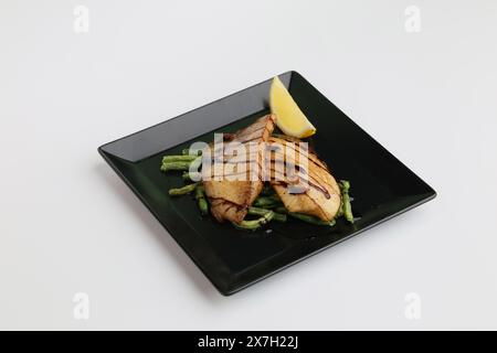 Gebackenes Weißfisch-Tilapia-Fischfilet auf schwarzer Platte isoliert auf weißem Hintergrund. Stockfoto