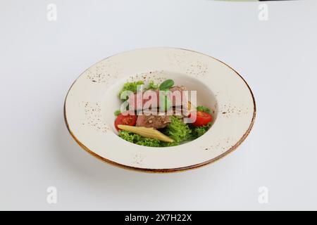 Thunfischsteak, Salat und Gemüse auf einem schönen Teller auf weißem Hintergrund, Restaurant serviert. Stockfoto