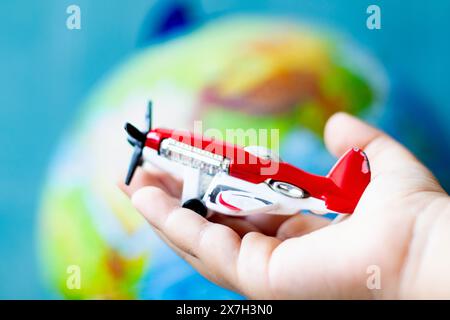 Die Kinderhand hält ein Spielzeugflugzeug mit einem Propeller in der Hand. Rotes Spielzeugflugzeug vor dem Hintergrund des Weltmodells. Konzept der Luftfahrtidee. Welttournee. Stockfoto