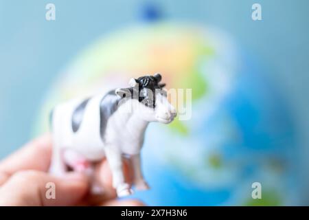 Plastikspielzeugkuh vor dem Hintergrund des Weltmodells. Kühe-Zucht und CO2-Emission-Ideenkonzept. Rinderhaltung. Methanemissionen aus der Tierhaltung. Stockfoto