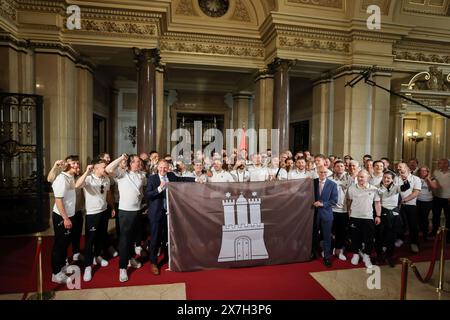 Hamburg, Deutschland. Mai 2024. Fußball: FC St. Pauli Promotion Party. Peter Tschentscher (SPD, Front r), erster Bürgermeister und Präsident des Senats der Freien und Hansestadt Hamburg, und Andy Grote (SPD, Front l), Senator für Inneres und Sport in Hamburg, hält eine braune Flagge mit dem Hamburger Wappen, ein Geschenk des Vereins, während er mit dem FC St. Pauli auf dem Spiegel im Rathaus steht. Quelle: Christian Charisius/dpa-Pool/dpa/Alamy Live News Stockfoto