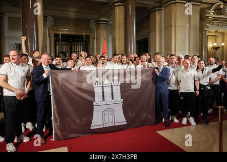 Hamburg, Deutschland. Mai 2024. Fußball: FC St. Pauli Promotion Party. Peter Tschentscher (SPD, Front r), erster Bürgermeister und Präsident des Senats der Freien und Hansestadt Hamburg, und Andy Grote (SPD, Front l), Senator für Inneres und Sport in Hamburg, hält eine braune Flagge mit dem Hamburger Wappen, ein Geschenk des Vereins, während er mit dem FC St. Pauli auf dem Spiegel im Rathaus steht. Quelle: Christian Charisius/dpa-Pool/dpa/Alamy Live News Stockfoto