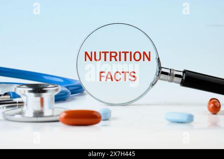 Viele Nutrition Facts Text geschrieben durch eine Lupe auf hellblauem Hintergrund, neben den Pillen Stockfoto