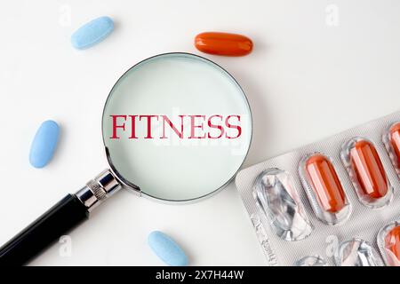 Fitness, gesunder Lebensstil und Sportkonzept: FITNESS geschrieben durch ein Lupenglas neben den Pillen Stockfoto