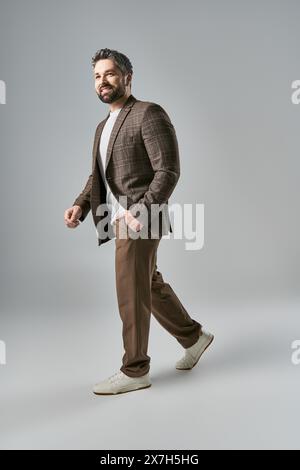 Ein stilvoller Mann mit Bart in einem eleganten braunen Anzug und weißem Hemd, der vor einem grauen Studio-Hintergrund posiert. Stockfoto