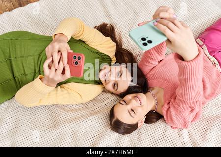 Zwei junge Frauen in lässiger Kleidung genießen einen Moment der Entspannung, während sie nebeneinander auf einem gemütlichen Bett liegen. Stockfoto