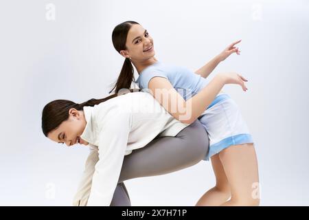 Zwei hübsche, brünette Teenager-Mädchen in sportlicher Kleidung zeigen ihre Tanzbewegungen in einem Studio vor grauem Hintergrund. Stockfoto