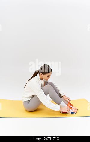 Ein hübsches, brünettes Teenager-Mädchen in Sportswear sitzt im Kreuz auf einer gelben Matte in einem Studio. Stockfoto