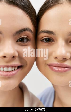 Zwei hübsche und brünette Teenagermädchen machen ein Selfie in einem Studio vor grauem Hintergrund. Stockfoto