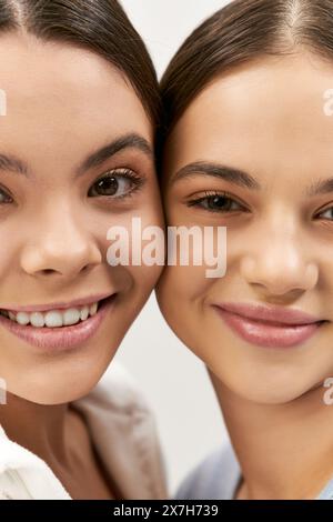 Zwei hübsche brünette Mädchen im Teenageralter lächeln und posieren für ein Foto in einem Studio vor grauem Hintergrund. Stockfoto