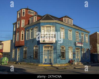 Zwei Männer sitzen vor einem bemalten viktorianischen Gebäude mit Metallummantelung in Castro auf Chiloe Island, Chile. Stockfoto