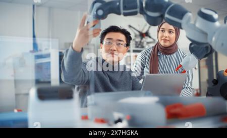 Arab Female Future Engineer beschäftigt sich mit der Arbeit eines geschickten Entwicklers. Asian man erklärt Grundprinzipien und Examine Robotic Arm. Analyse und Evaluation von Prototypen und Robotersystemen. Stockfoto