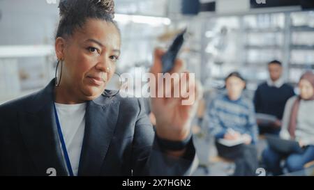 Black Female Teacher schreibt lange und komplexe mathematische Formel-Gleichung auf dem transparenten Board während der Vorlesung mit verschiedenen Studenten. Konzept der Technischen Universität. Point of View im Hochformat. Stockfoto