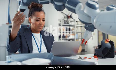 Porträt einer schwarzen weiblichen Senior Engineerin, die am Engineering Project, Codierung auf Laptop und Änderung der Roboterhandposition im modernen Büro arbeitet. Befähigte Wissenschaftler mit kreativem Projekt. Stockfoto