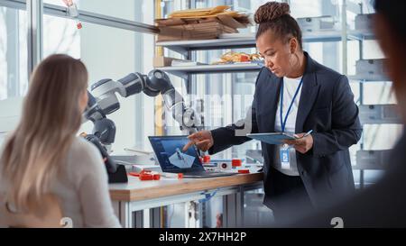 Weibliche Informatikspezialistin mit Schwerpunkt auf Intersting Lecture von afroamerikanischer Professorin. Verschiedene Gruppe junger Ingenieure, die Roboterhand programmieren. Advanced Robotics Class Konzept. Stockfoto