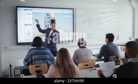 Univ.-Robotik-Vortrag: Schwarzer Lehrer erklärt den Studenten Technik. Sie Verwendet Interaktives Whiteboard. Verschiedene Gruppen junger Ingenieure hören in der Klasse über die Programmentwicklung für Robotic Arm. Stockfoto