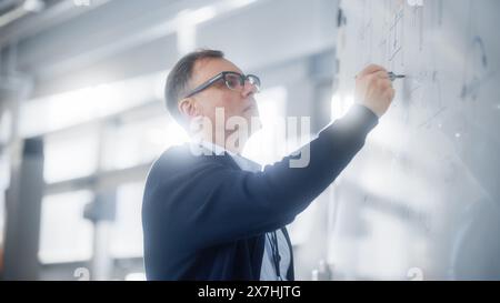 Der Lehrer spricht mit den Schülern und verwendet das Schwarze Brett während der Universitätsvorlesung im Klassenzimmer. Der kluge Kaukasier zeichnet Formeln und Pläne auf dem Seminar. Genius Löst Probleme Konzept. Stockfoto