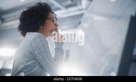Schwarze Wissenschaftlerin löst Probleme und schreibt komplizierte mathematische Gleichungen auf dem Whiteboard. Genius, Konzeptualität und Durchbruch in Wissenschaft und Technologie. Stockfoto