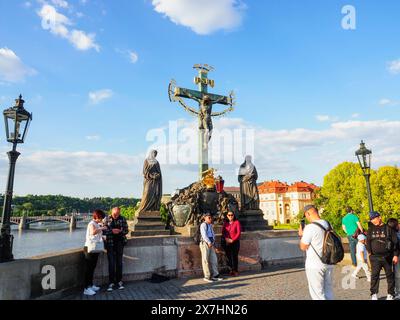 Prag, Tschechische Republik - 10. Mai 2024: Touristen machen Fotos in der Nähe der schönen Bronzestatue der Kreuzigung Jesu Christi. Statue des Heiligen Stockfoto