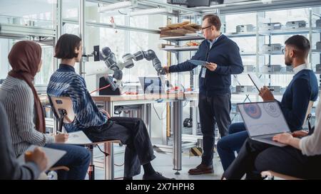 Männlicher Professor, der mit Laptop steht und verschiedenen Studenten die Kontrolle der Roboterhand erklärt. High-Tech-Forschungslabor mit moderner wissenschaftlicher Ausrüstung. Workshop Startup Lab Konzept. Stockfoto