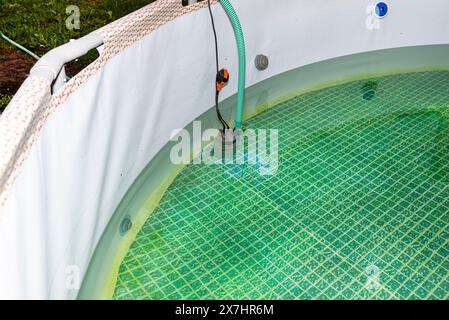 Entleeren von gebrauchtem Wasser aus einem Garten-Swimmingpool mit einer Hauswasserpumpe. Stockfoto