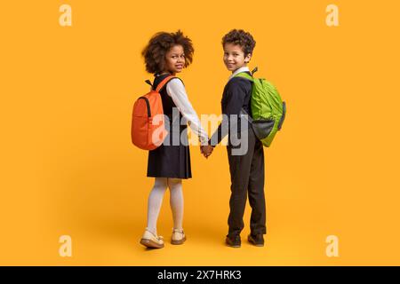 Zwei Kinder, die Hände mit Rucksäcken auf gelbem Hintergrund halten Stockfoto