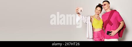 Ein stilvolles junges Paar, das einen Moment zusammen mit einem Handy vor grauem Hintergrund festnimmt. Stockfoto