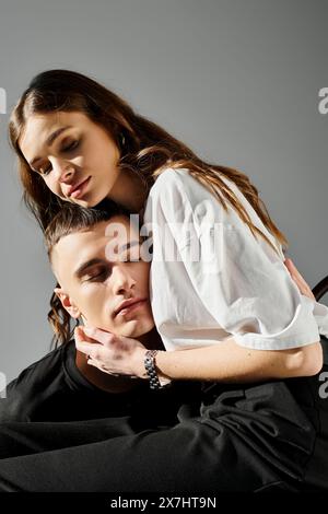 Ein junger Mann hält eine Frau auf dem Rücken vor grauem Hintergrund, zeigt Stärke und Zuneigung. Stockfoto