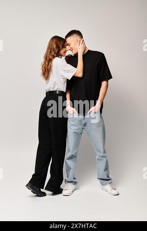 Ein junges Paar, tief verliebt, steht Seite an Seite in einem Studio vor grauem Hintergrund. Stockfoto