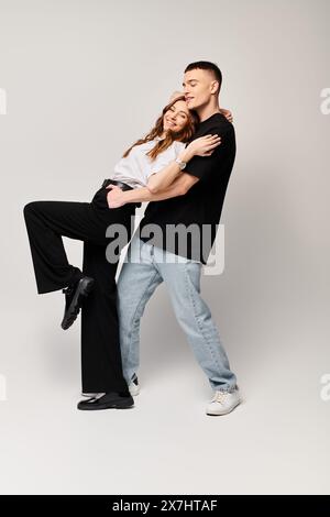 Ein junger Mann und eine junge Frau posieren zusammen und strahlen Liebe und Stil vor grauem Hintergrund in einem Studio aus. Stockfoto